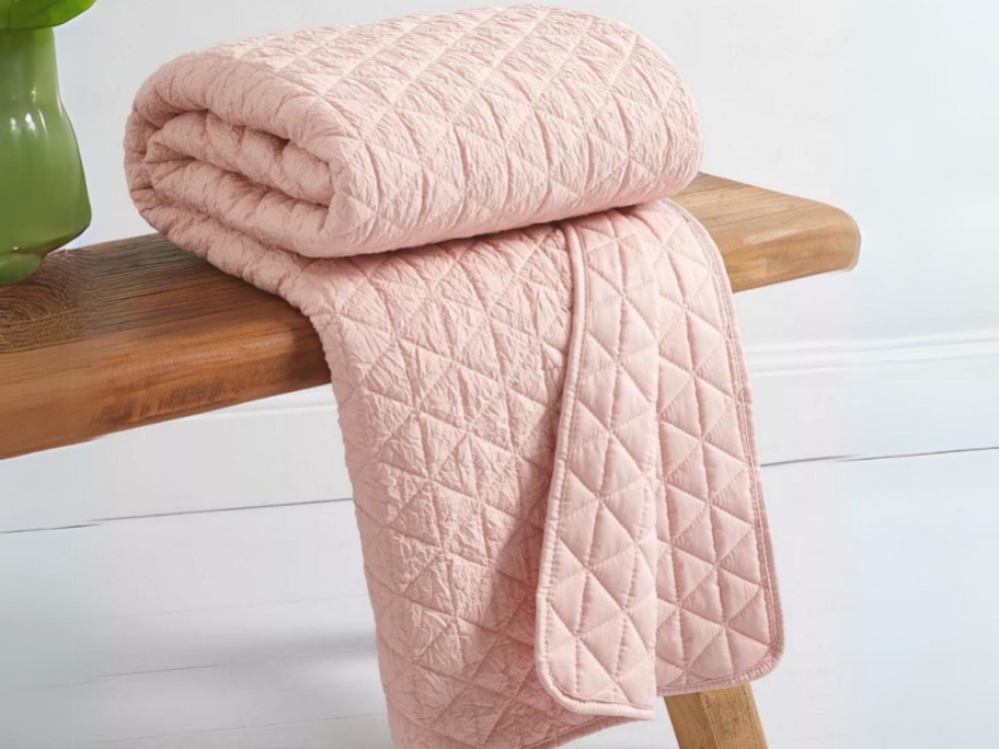 pink quilted throw blanket folded on a bench