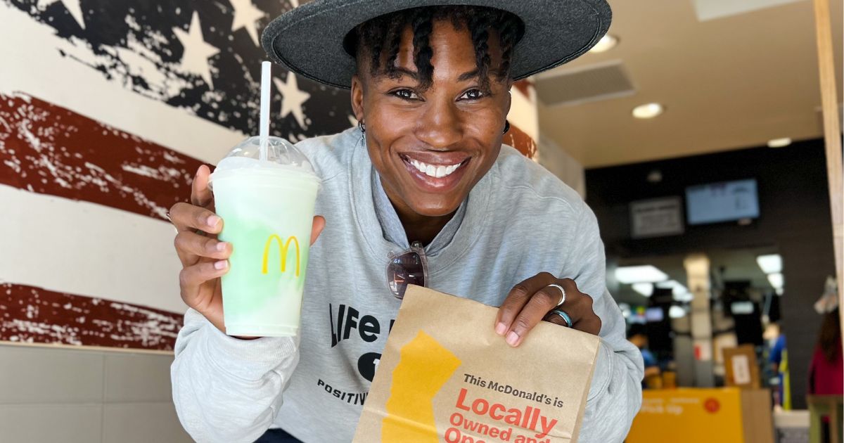 a woman smiling and holding a shamrock shake in one hand and a brown paper mcdonalds bag in the other