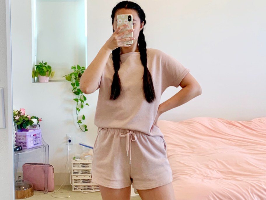 woman taking photo of herself wearing pink lounge set shirt and top in living room