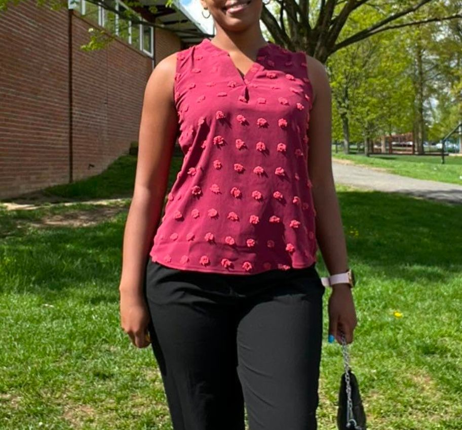 woman in a burgundy tank top and black pants standing outside