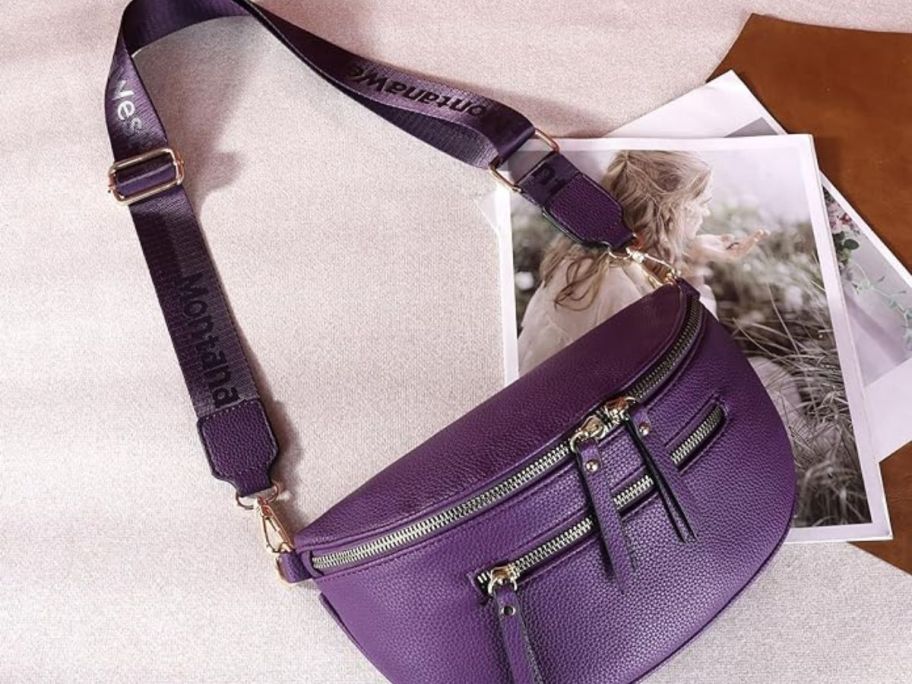 Montana West Crossbody Bags for Women Designer Sling Bag with Adjustable Strap laying on table with strap stretched out in purple