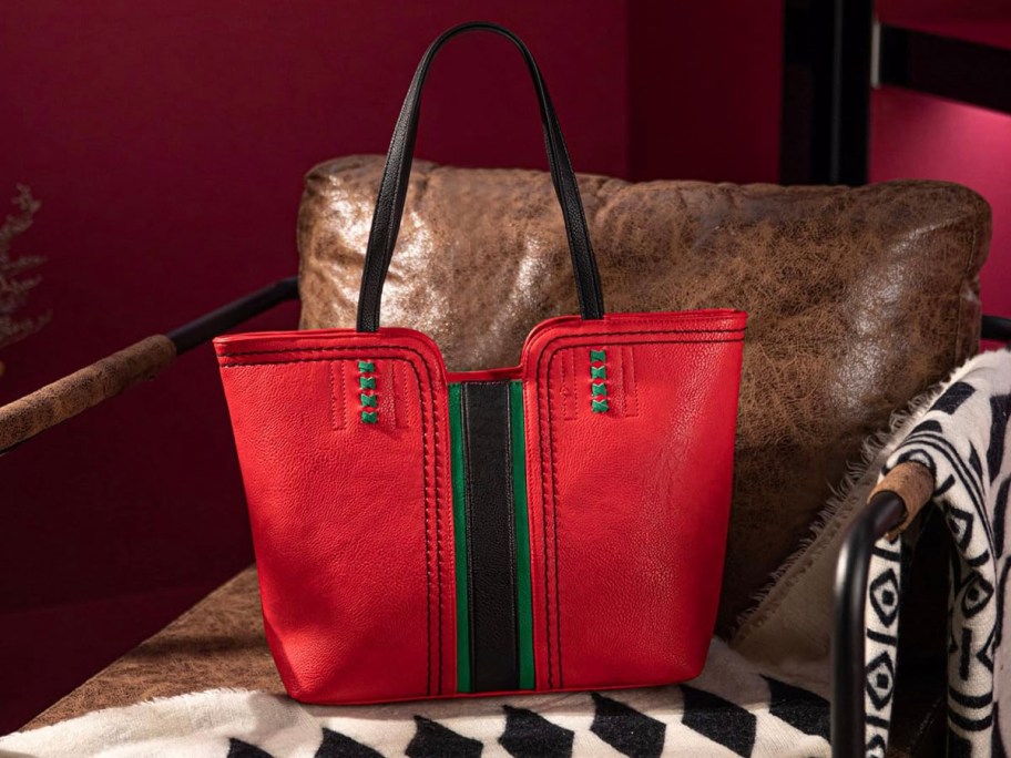 red and black vegan leather tote sitting on brown leather couch