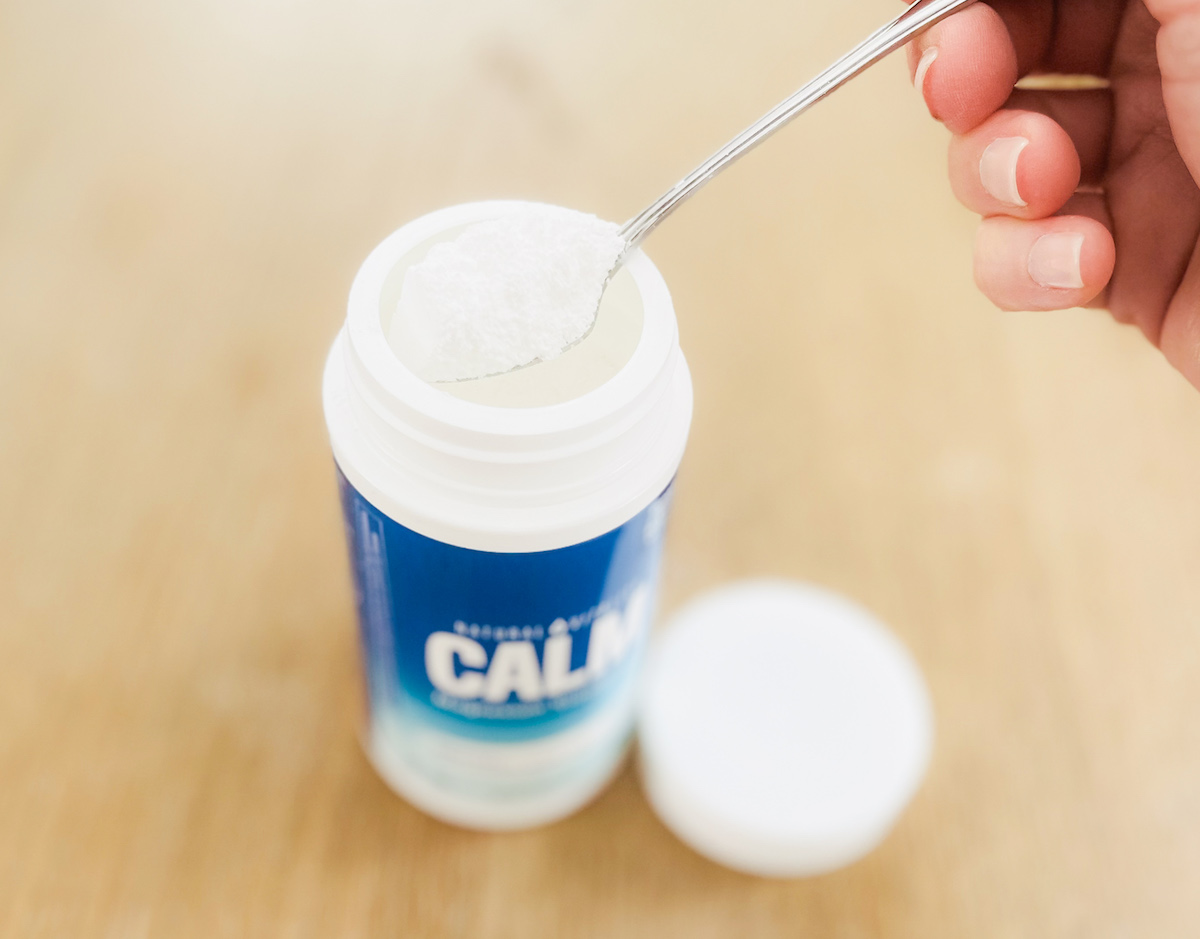 top of open calm magnesium container with hand holding silver spoonful 