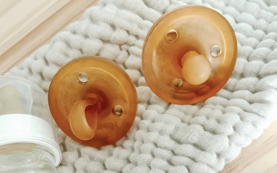 two natursutten brown rubber pacifiers on baby blanket