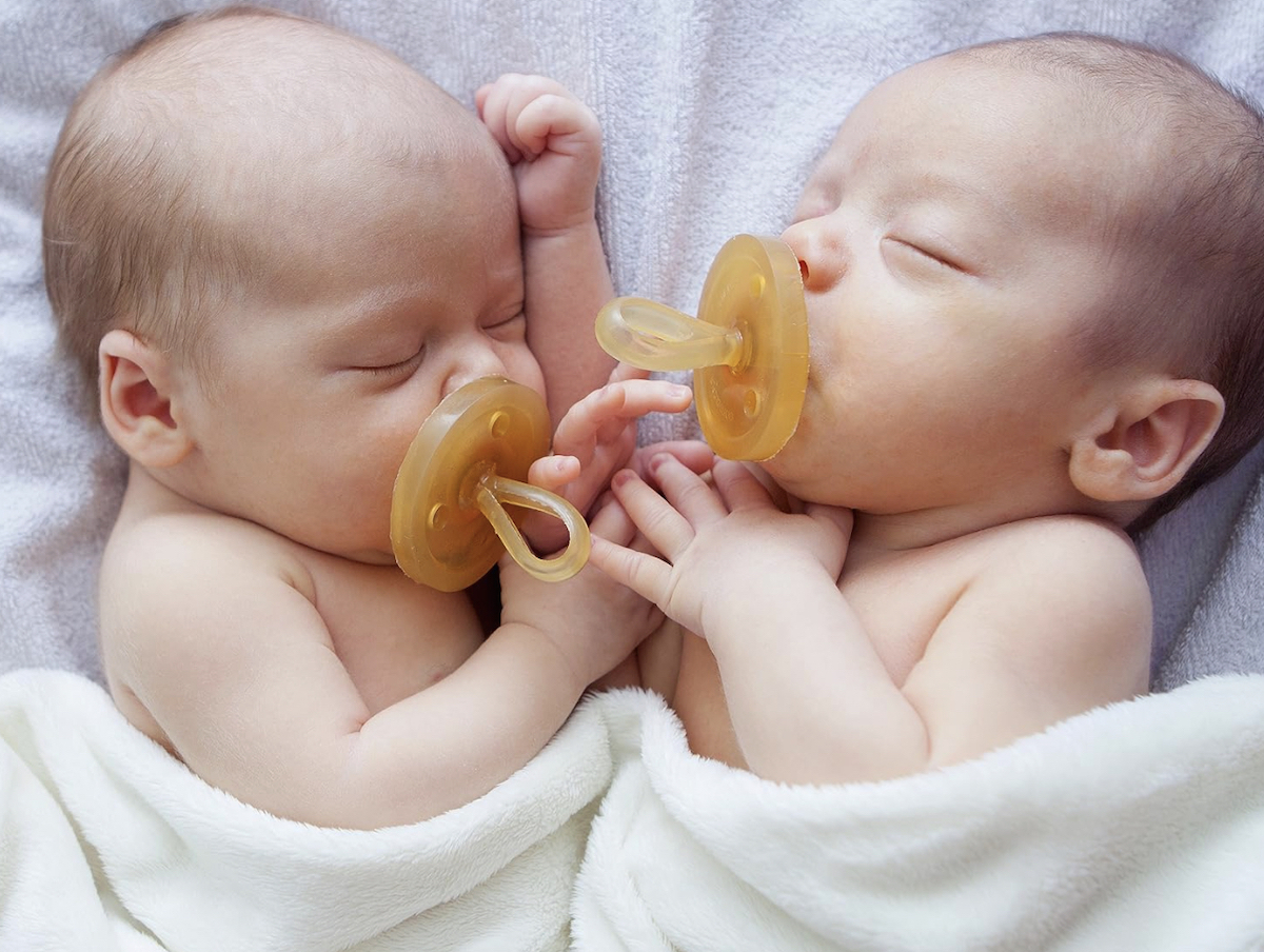 two newborn babies sleeping with rubber pacifiers and white blanket