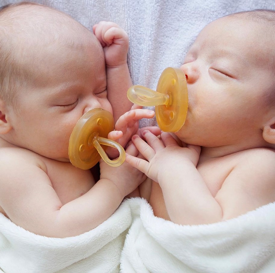 two newborn babies sleeping with rubber pacifiers and white blanket