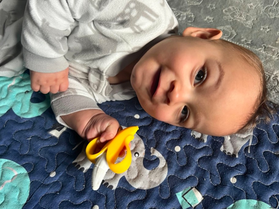 baby laying down holding banana teether