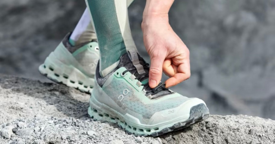 person wearing green on running shoes fixing shoelace
