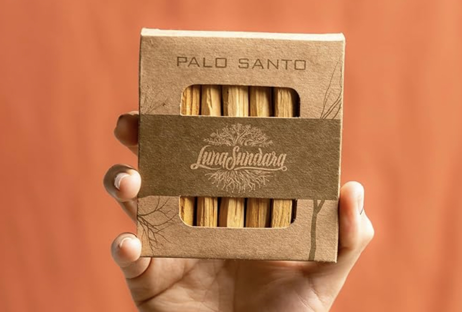 hand holding a pack of palo santo sticks in box with orange background
