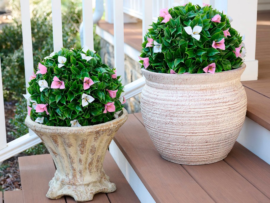 two faux sphere plants with pink flowers in pots on stairs