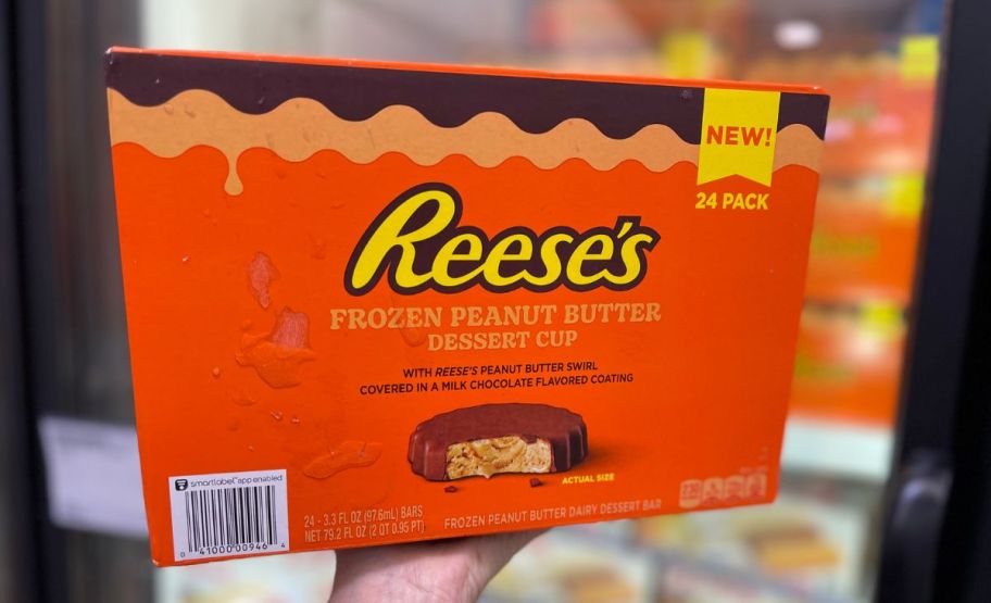 a womans hand holding up a box of reeses frozen peanut butter cups in a sams club