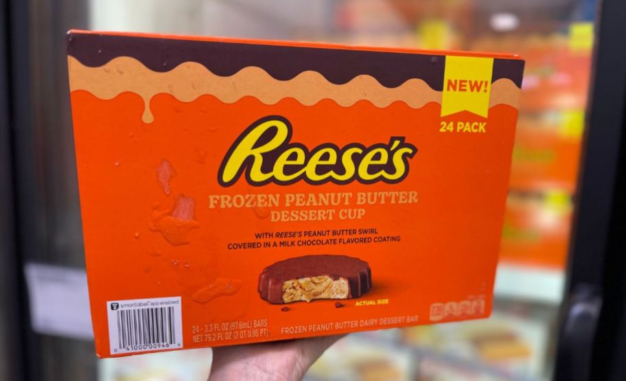 a womans hand holding up a box of reeses frozen peanut butter cups in a sams club
