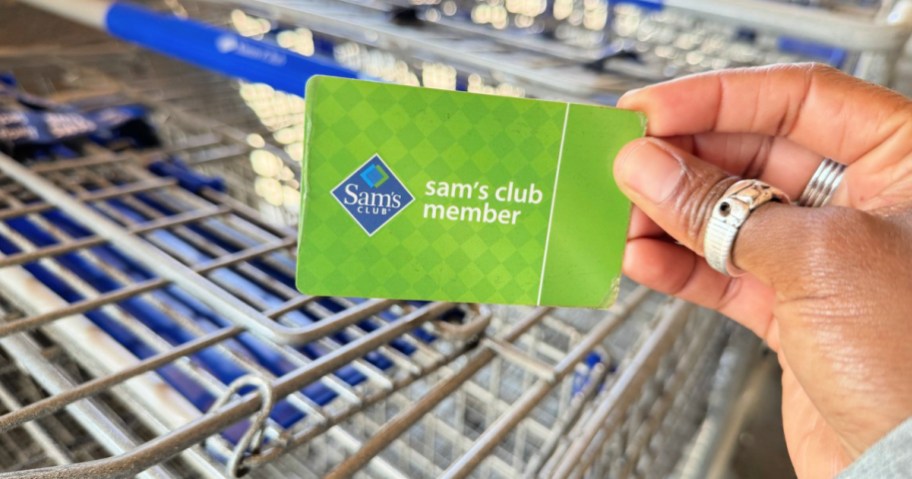 sam's club membership card in-hand in front of shopping carts