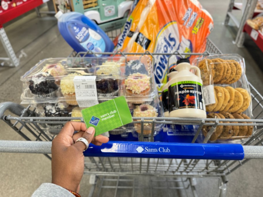 sams club cart full of products with a hand holding a membership card above it