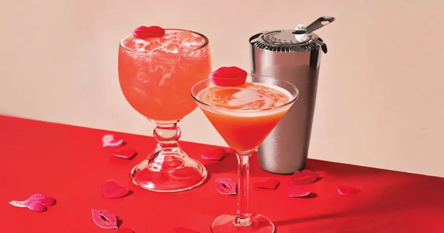 two cocktails next to a silver shaker on a red tablecloth