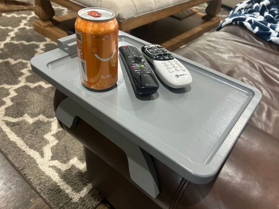 grey sofa arm tray on a brown sofa with remotes and a canned drink