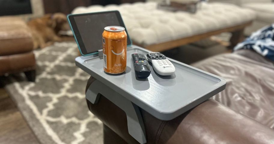 grey sofa arm tray on a brown sofa with remotes, canned drink and tablet on it