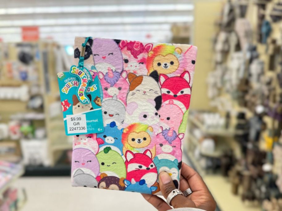 hand holding up a plush journal with various Squishmallow characters on it