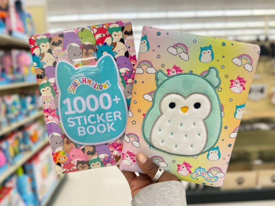hand holding up a Squishmallows sticker book and activity journal with Squishmallow characters on them