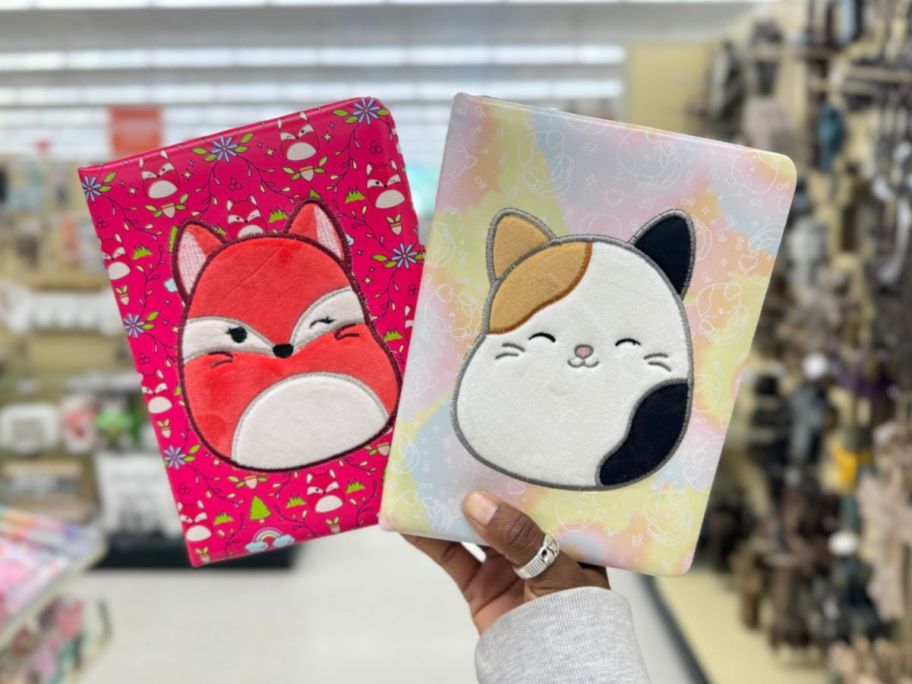 hand holding up 2 different plush Squishmallow journals