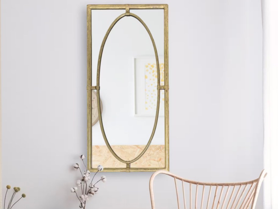 gold rectangle mirror with accents hanging on wall above a flower and chair