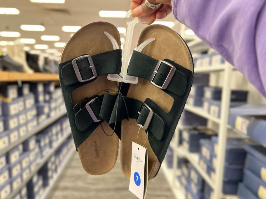 hand holding a pair of men's black and tan footbed sandals in a Target aisel
