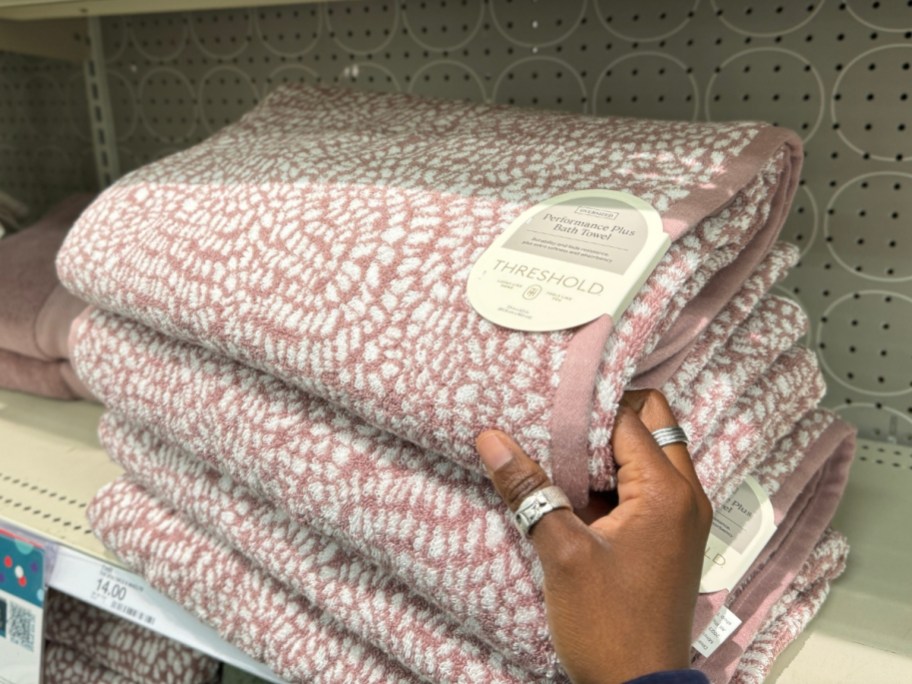 hand reaching for a pink patterned bath towel on a shelf