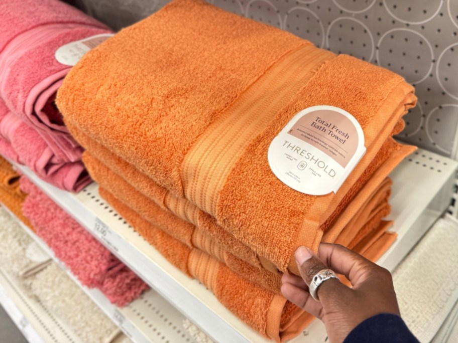 hand reaching for a large orange bath towel on a shelf
