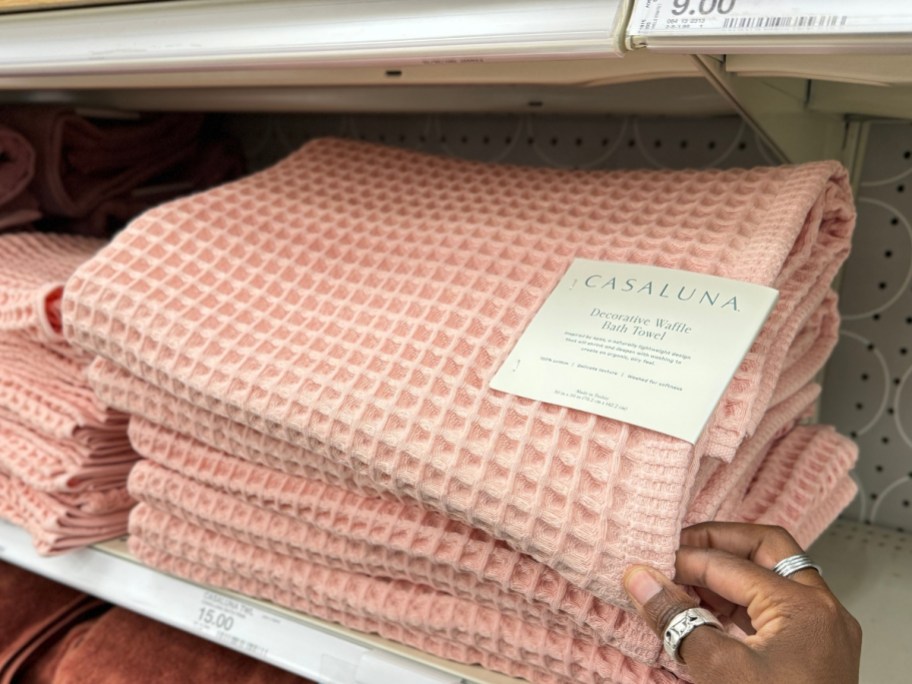 hand reaching for a light pink waffle bath towel on a shelf