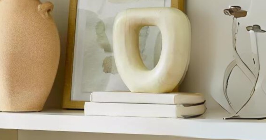 rounded off white teak wood modern sculpture on a bookshelf