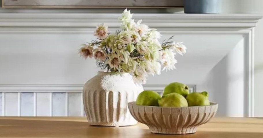 ceramic carved round vase with flowers in it, sitting behind a bowl of green apples