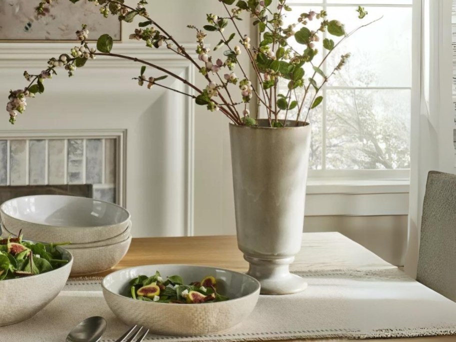 dining table with bowls of food and a ceramic rustic looking flower vase with flowers