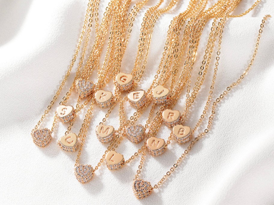lots of gold initial necklaces sitting on white sheet
