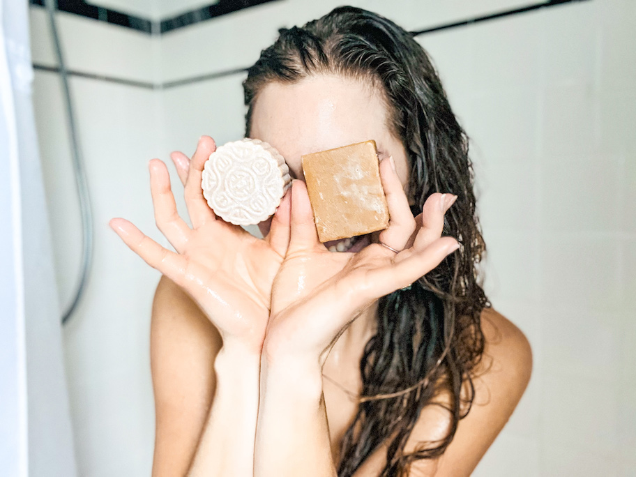 woman holding bar shampoo and conditioner in shower in front of face