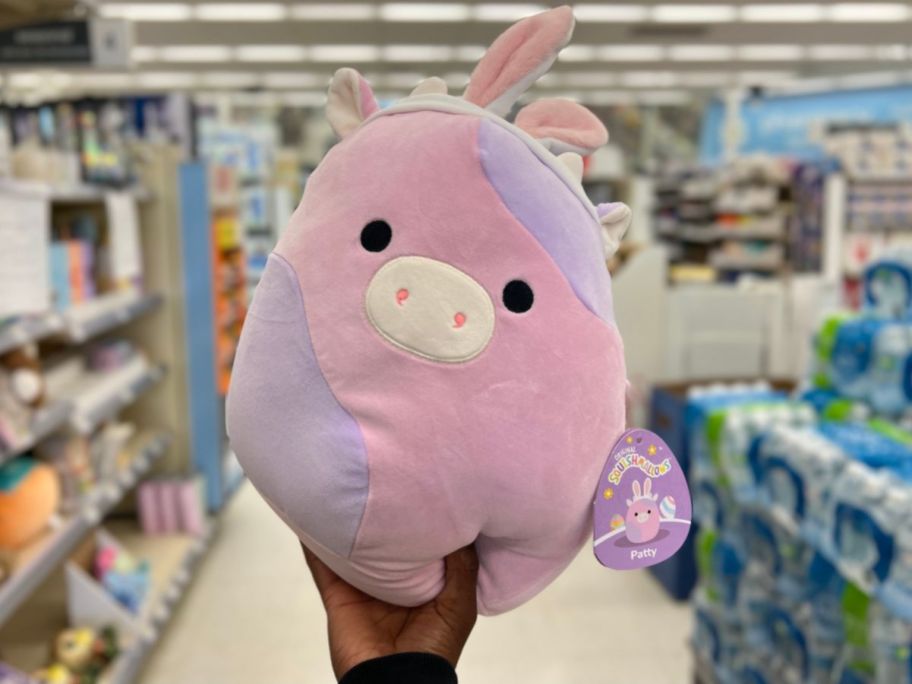hand holding a pink and purple Squishmallows Cow With Bunny Ears