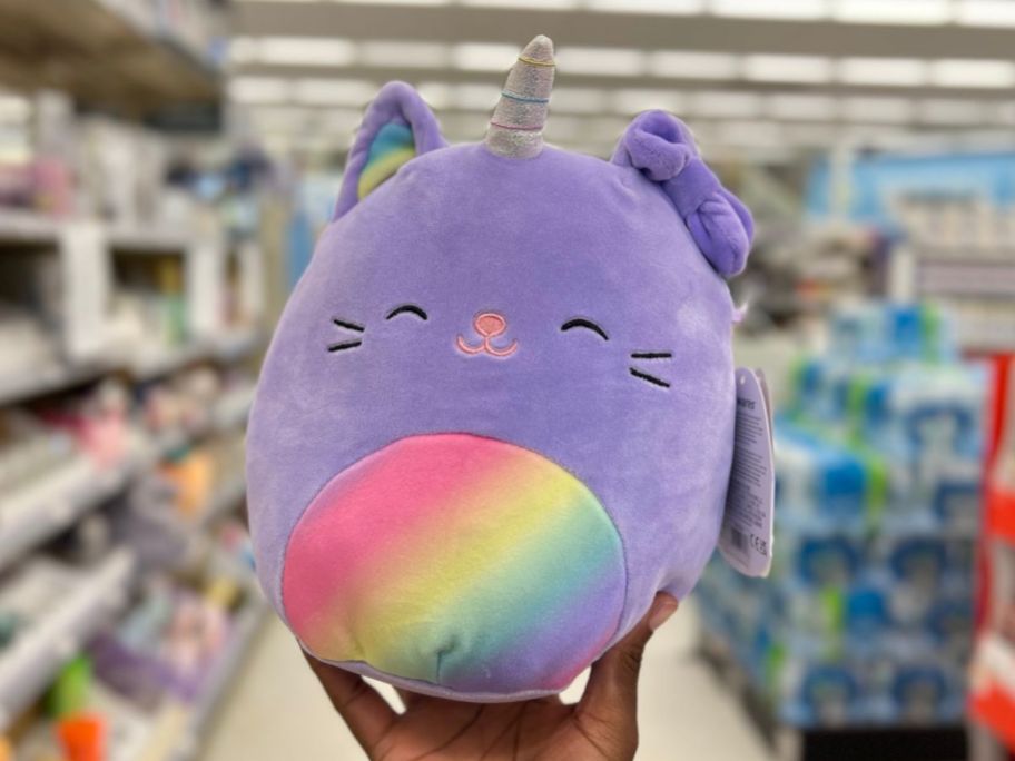 hand holding a purple Squishmallows caticorn with a rainbow belly