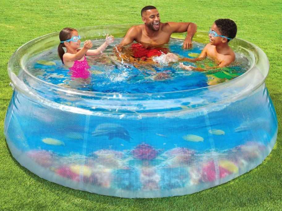 A man and two kids sitting inside a transparent inflatable pool