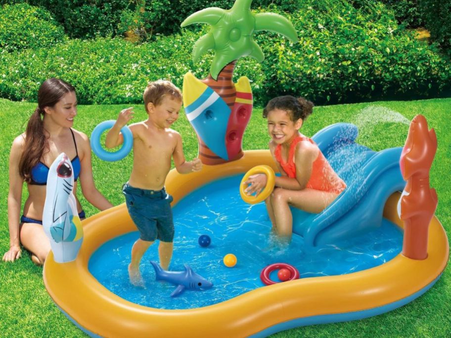 two kids playing in a beach-themed inflatable pool with a mom sitting nearby