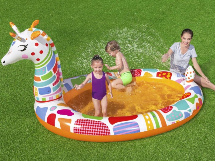 Inflatable giraffe pool with two kids playing in it and mom sitting nearby