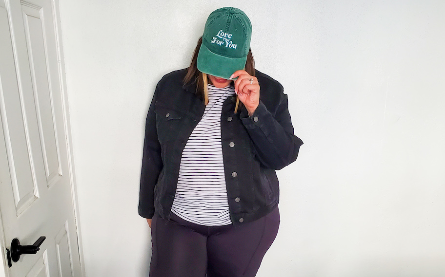 woman wearing green baseball hat and black denim jacket in front of white wall