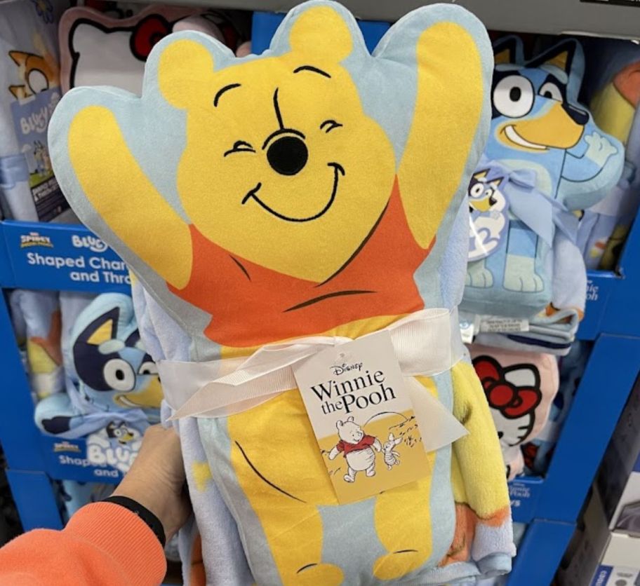 a womans hand holding a winnie the pooh pillow and throw set