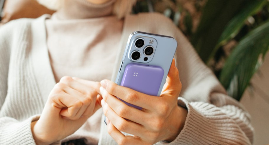 woman holding her iPhone with a purple power bank attached to the back of it while siting down