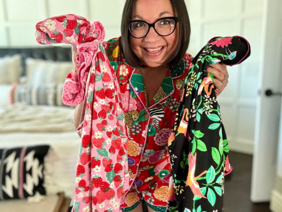 a woman wearing a pair of tropical print pajamas and holding additonal set in both hands