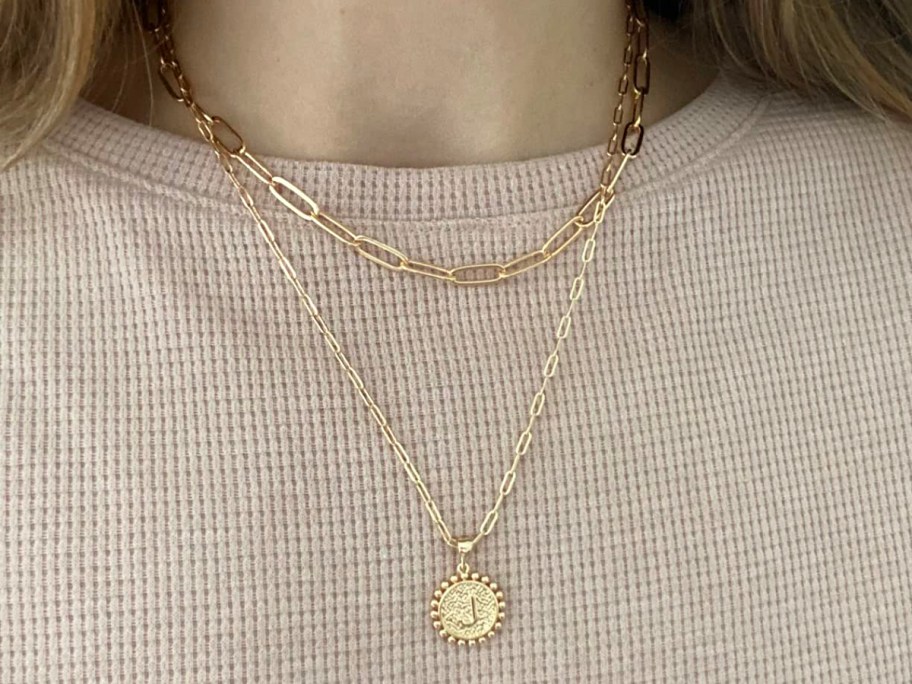 woman wearing layered gold initial necklace over beige shirt