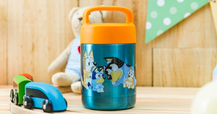 bluey food jar with orange lid sitting on table next to toys