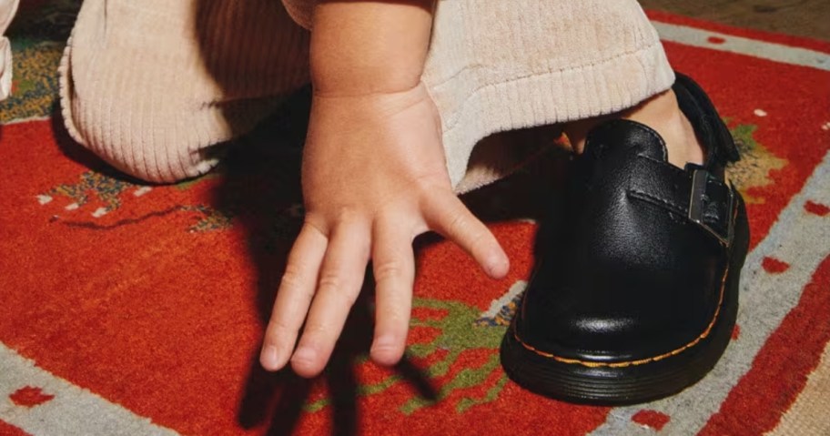 toddler reaching for the ground wearing black Dr. Martens mules