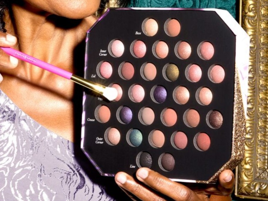 woman holding an eye shadow palette and brush