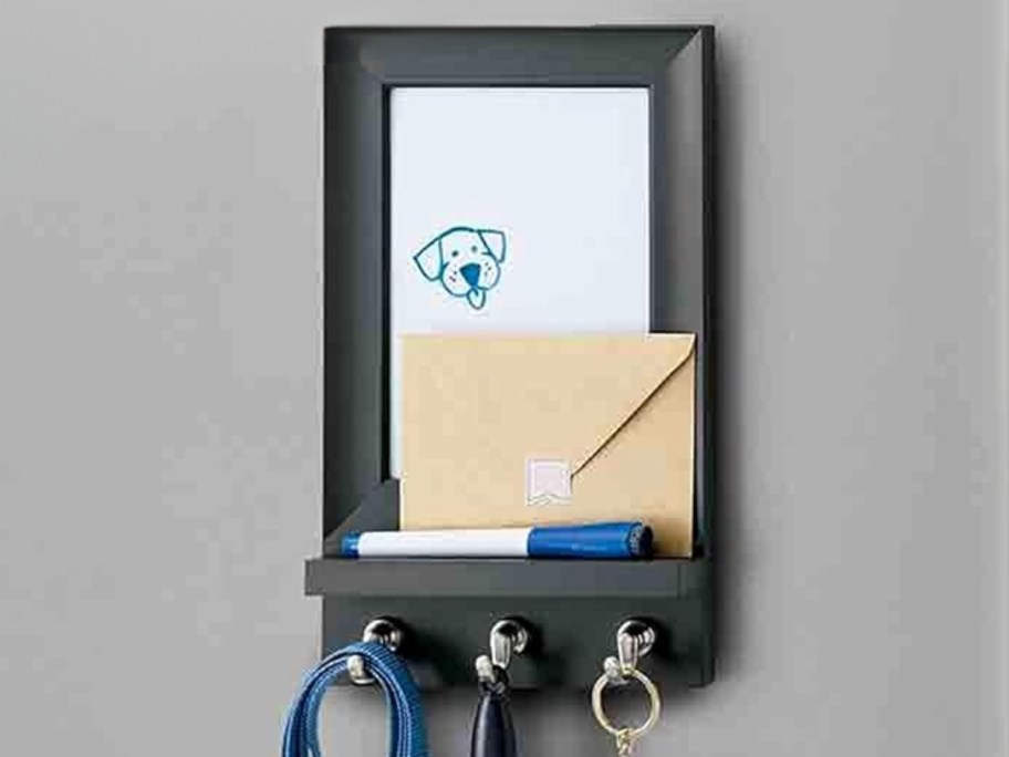 black framed dry erase board with key hooks on wall with mail, dry erase marker and keys on the hooks