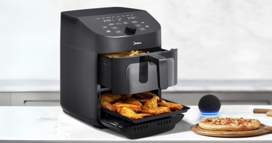 black dual air fryer with open drawer and basket and food in it, sitting next to a pizza and an Alexa device