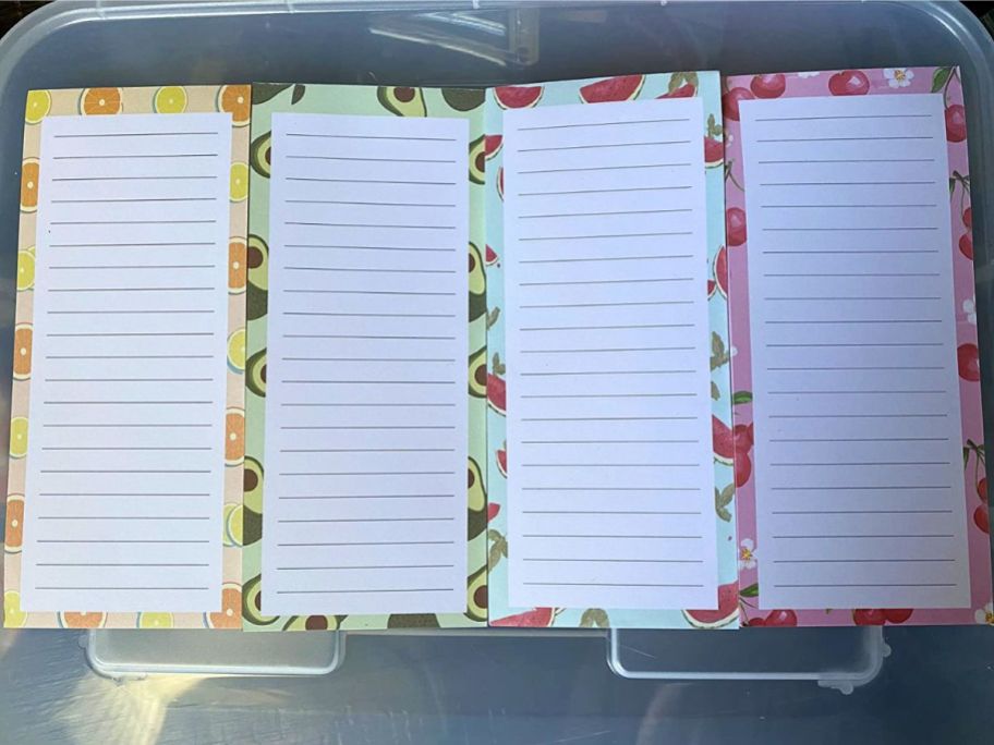 4 different shopping list style magnetic notepads with fruit borders laid out on container